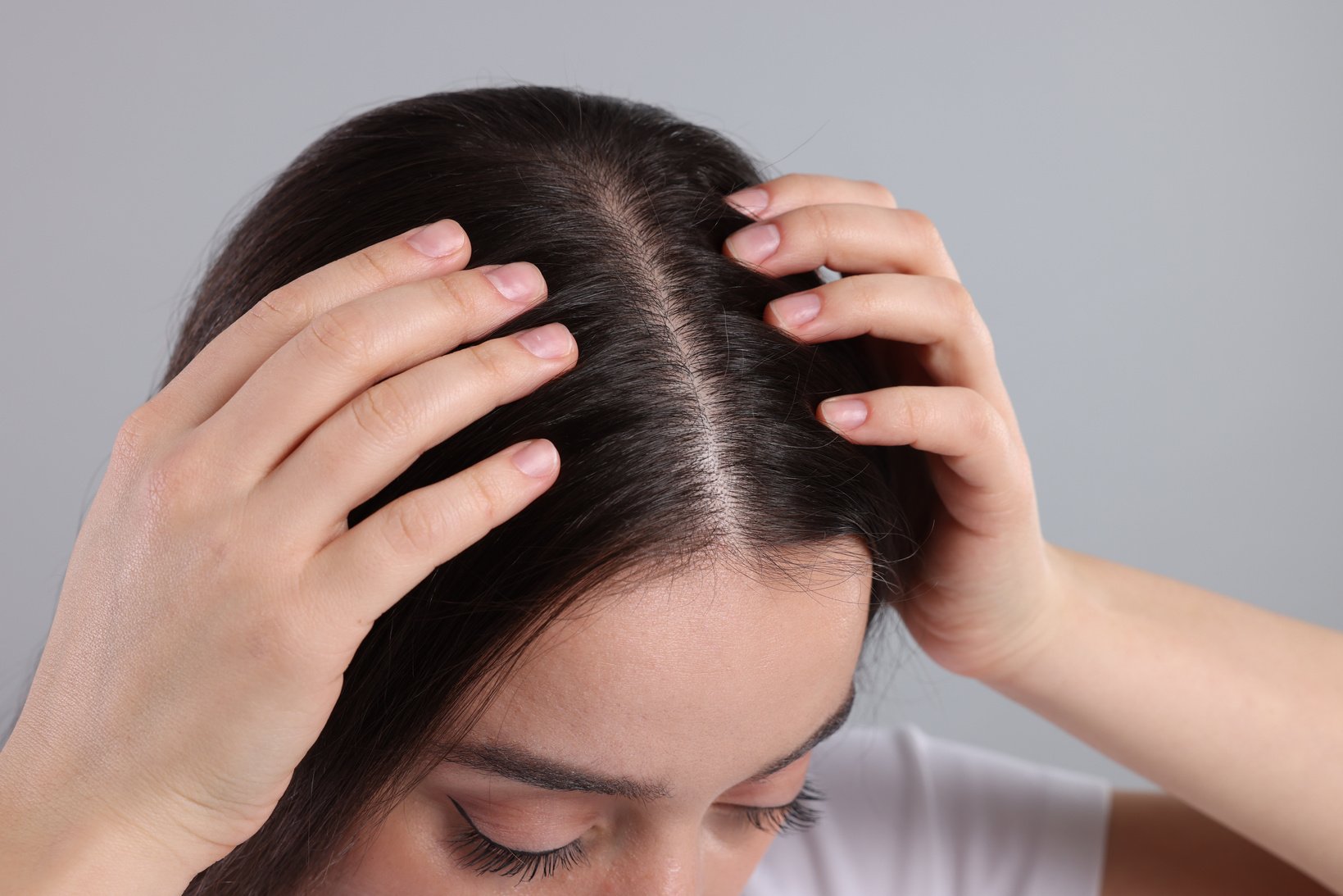 Woman Examining Her Hair and Scalp on Grey Background, Closeup